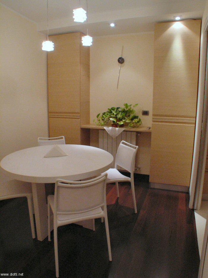 Vista d'insieme della sala da pranzo con le colonna contenitori con fianchi personalizzati in rovere sbiancato. Bellissimi la lampada a sospensione e l'orologio minimal. Comode e raffinate le sedie Yang di Bontempi in polipropilene e texplast bianchi abbinate ad un tavolo in rovere laccato a poro aperto bianco (realizzato da un artigiano cugino del nostro cliente).
